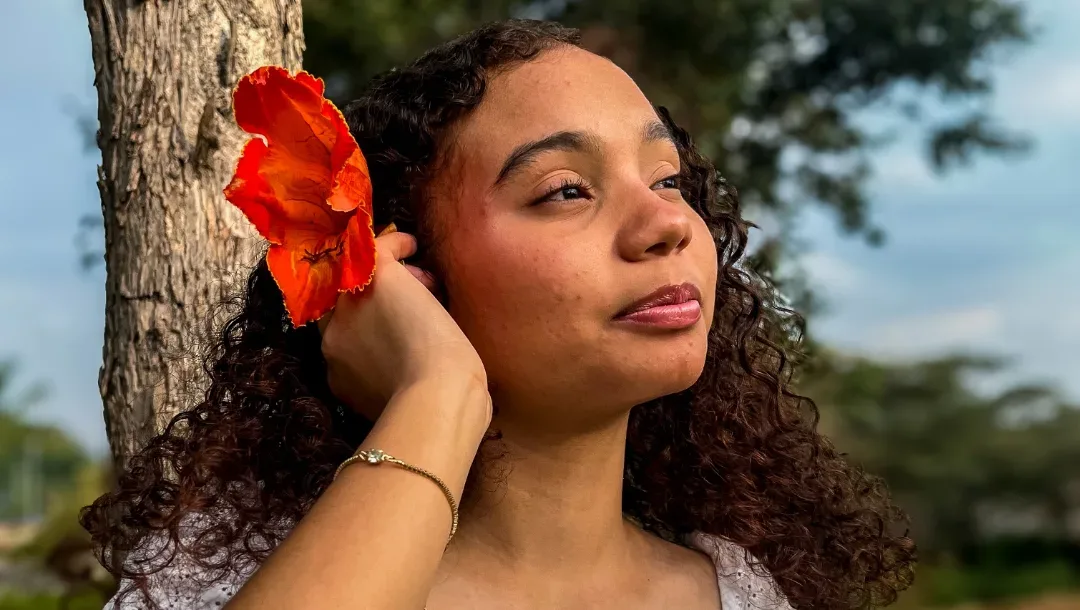 Jovem de cabelo cacheado com uma flor vermelha no cabelo, em ensaio ao ar livre.